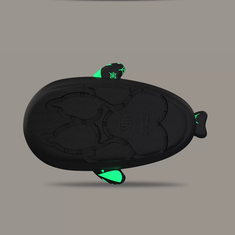 Bottom outsole view of black Halloween shark slides demonstrating the wave-pattern anti-slip grip and non-slip tread, flanked by glowing green side fins. Bottom tread view of anti-slip black Cloudsharks Halloween shark slides featuring a textured grip sole and glowing green side fins.