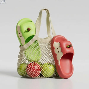 Studio product shot of red and green Apple Cloud Slides resting against a woven mesh tote bag with apples, comfortable shark slippers alternative.
