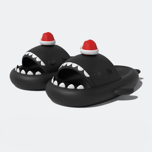 Full pair of black shark slippers with prominent white teeth and a small red Santa hat, isolated on a white background.