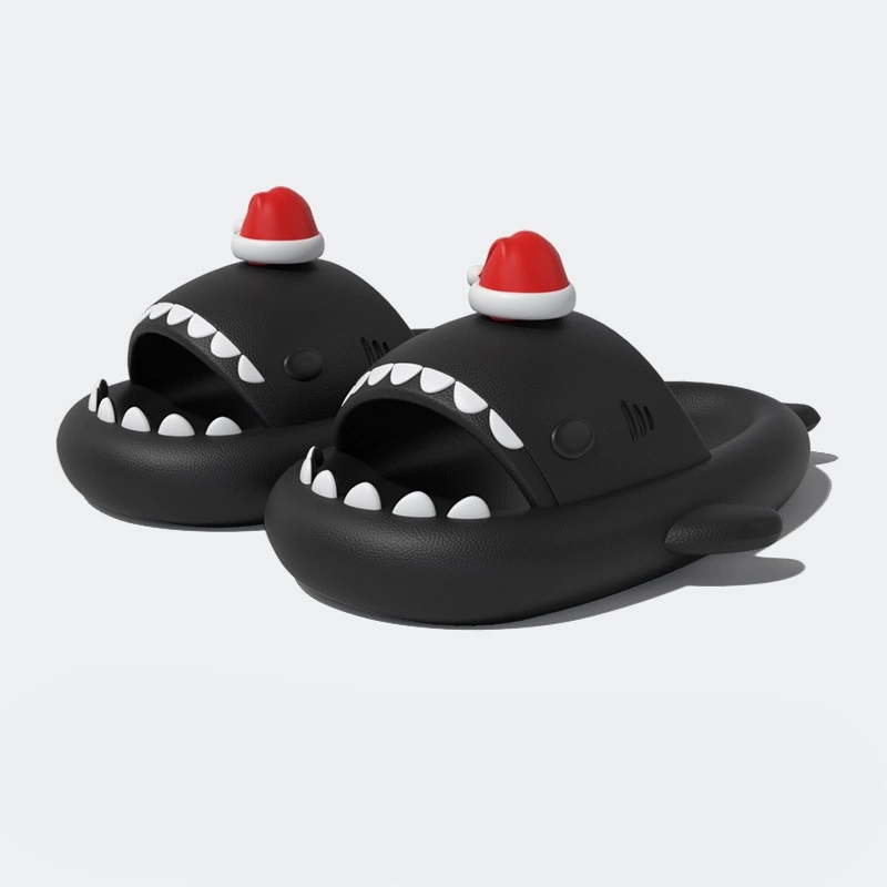 Full pair of black shark slippers with prominent white teeth and a small red Santa hat, isolated on a white background.