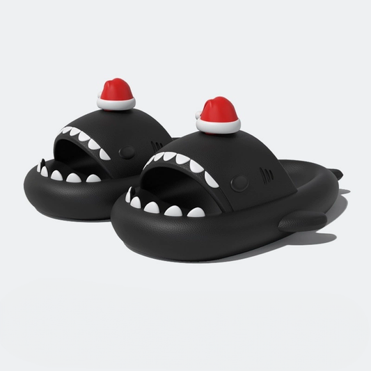 Full pair of black shark slippers with prominent white teeth and a small red Santa hat, isolated on a white background.