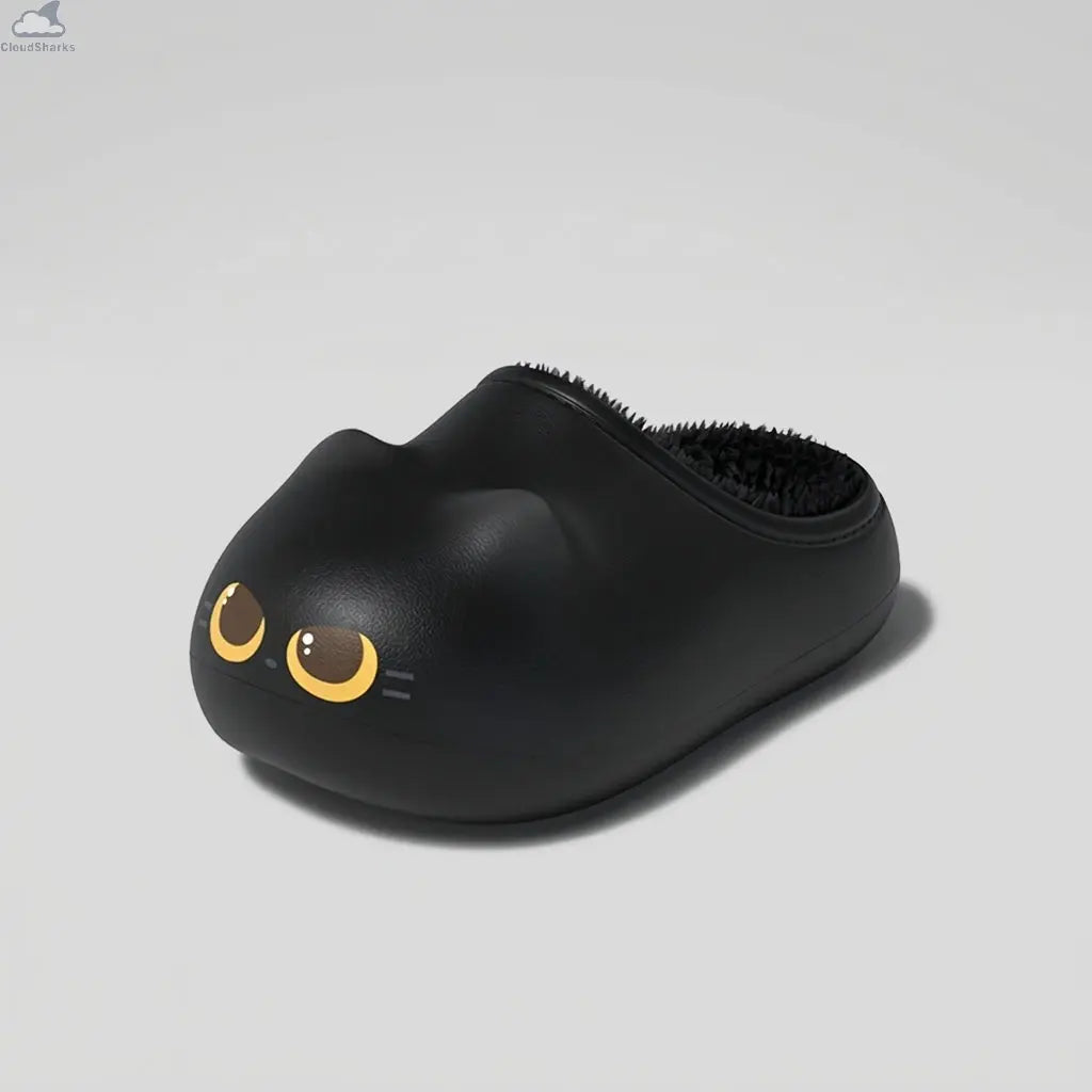 Three-quarter angle view of a black Cloudsharks cat slipper showing its rounded clog shape, matte EVA texture, cat-ear bump, and golden cat eyes on a light grey studio background.
