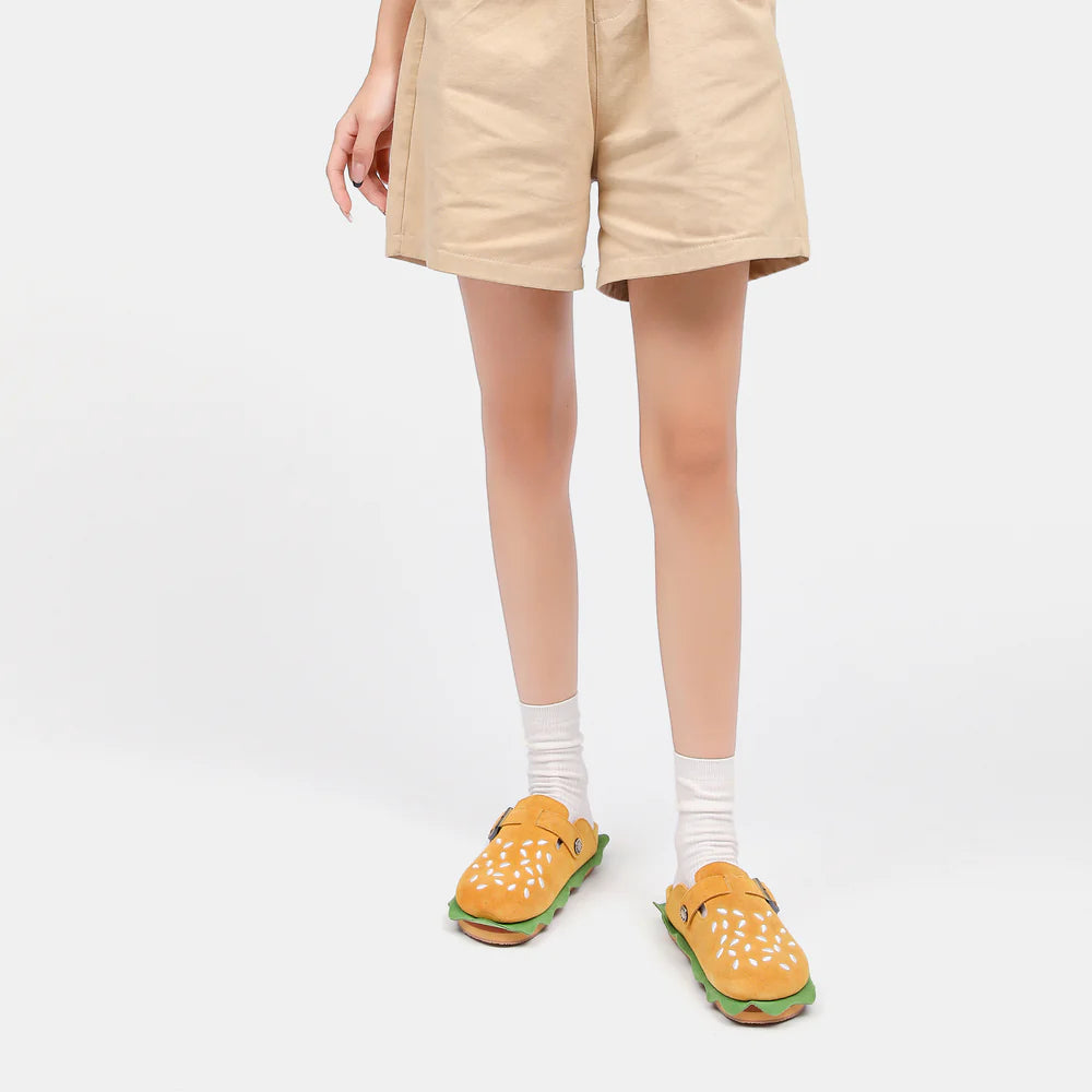 A full-body shot of a model wearing a tan Cloudsharks Friends t-shirt and shorts paired with burger slippers, offering a cozy lifestyle alternative to original shark slides.