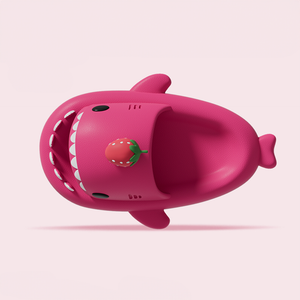 An angled front view of a single whimsical pink Cloudshark shark slipper. The image highlights the playful design, including the open mouth, white teeth, and a cute strawberry charm.