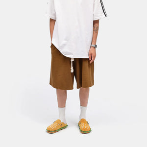 A person wearing an oversized white t-shirt and brown shorts modeling the burger slippers, offering a unique twist for lovers of shark slides and comfortable slides.