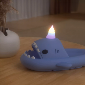 A blue Unicorn Shark Slide with a glowing rainbow unicorn horn, resting on a wooden surface next to a white vase. The scene is dim, emphasizing the luminous effect of the horn.