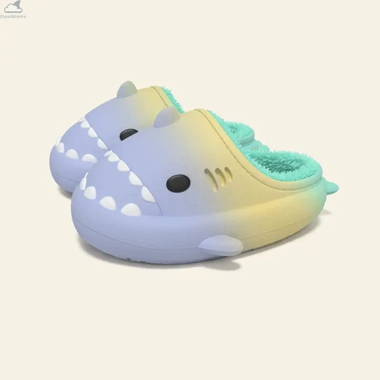 Pair of pastel blue and yellow gradient shark slides featuring plush mint green fleece lining, non-slip cloudsharks waterproof slippers. A pair of Gradient Winter Shark Slides featuring a blue-to-yellow outer body with mint green plush fleece lining resting on a neutral background.