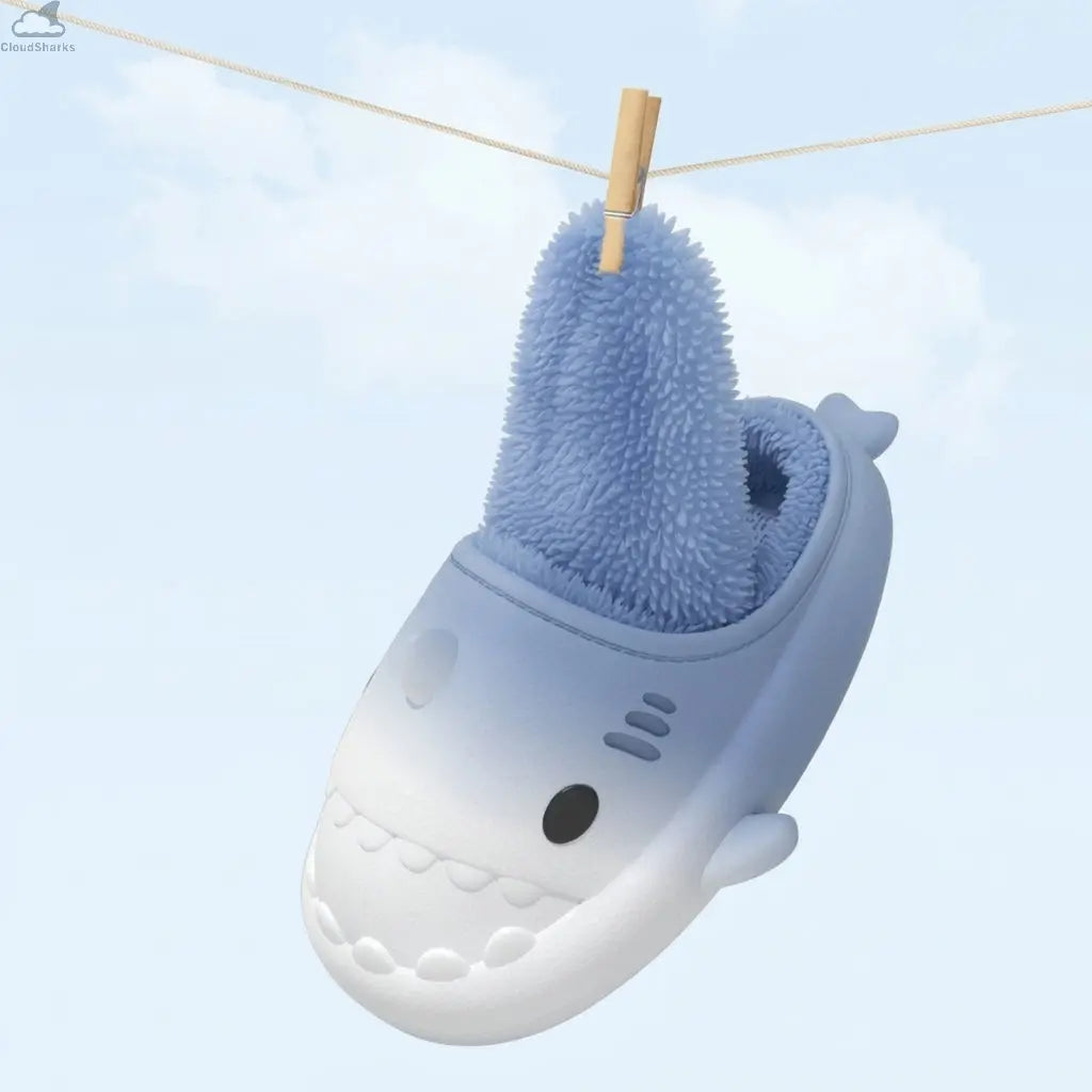 Single blue gradient winter shark slide hanging on a clothespin showcasing its removable plush fleece lining for quick drying, cloudsharks cozy house slippers.A single light blue to white gradient shark slipper hanging on a clothesline with a wooden clothespin, demonstrating its removable plush fleece inner lining pulled upwards for easy cleaning and drying.