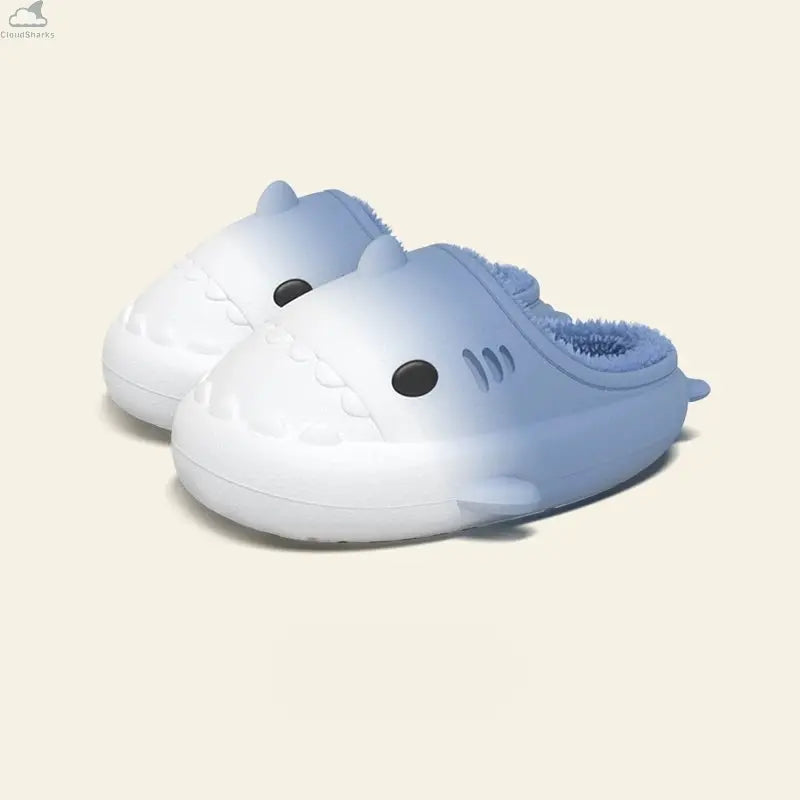 Pair of white to light blue gradient shark slippers with soft fluffy fleece interior, cute cloudsharks plush house shoes. A pair of Gradient Winter Shark Slides in a clean white-to-light-blue colorway with matching fluffy blue fleece lining.