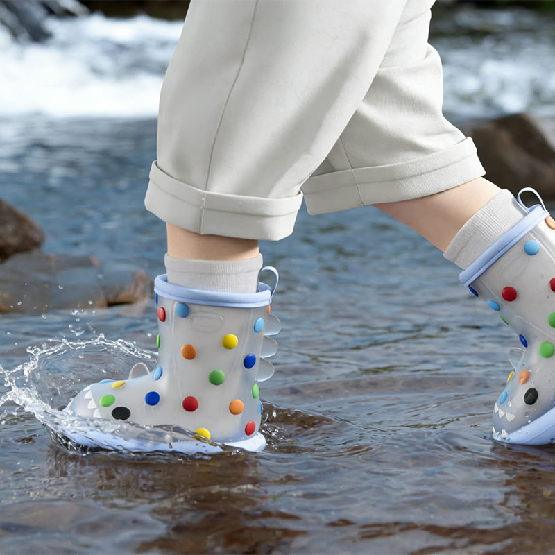 Toddler splashing in rainbow polka dot shark rain boots, cute waterproof kids shark boots with colorful dots, ideal for rainy outdoor exploration and puddle play.
