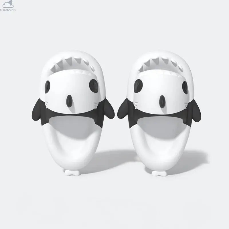 Top-down view of the pair of black and white Panda Shark Slides with a clean snout design, highlighting the inner footbeds, side fins, and shark teeth. Top-down view of white and black Cloudsharks Panda Shark Slides showing wide open-toe shark mouths with sharp teeth and comfortable cushioned footbeds.