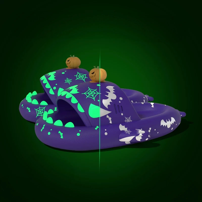 Purple Cloudsharks glow in the dark Halloween shark slippers with bat graphics, glowing teeth, and 3D pumpkin charms in daytime and nighttime lighting. Purple Halloween Shark Slides featuring a 3D jack-o'-lantern pumpkin charm topper, bat and spiderweb patterns, and glowing green accents displayed in a split-screen view.