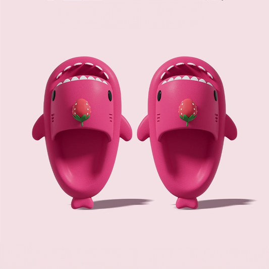 A top-down view of a pair of bright pink Cloudshark shark slides. Each slipper features a cute open mouth with white teeth, side fins, and a red strawberry charm on the strap.