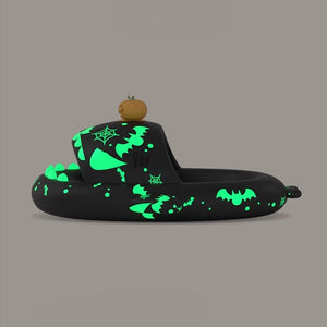 Side-profile view of black Halloween shark slides showcasing glowing green bat patterns, spiderwebs, illuminated teeth, side fins, and a 3D pumpkin topper. Side view of black Cloudsharks glow in the dark Halloween shark slides featuring glowing green bats, cobwebs, teeth, and a 3D pumpkin charm.