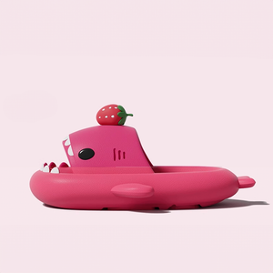 The side profile of a single pink Cloudshark shark slipper, showcasing its thick, cushioned sole for comfort, a small side fin, a black eye, and a decorative strawberry on top.
