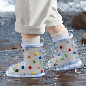 Child walking through water in rainbow dot shark rain boots, lightweight polka dot design with shark teeth, non-slip sole, perfect for rainy adventures.