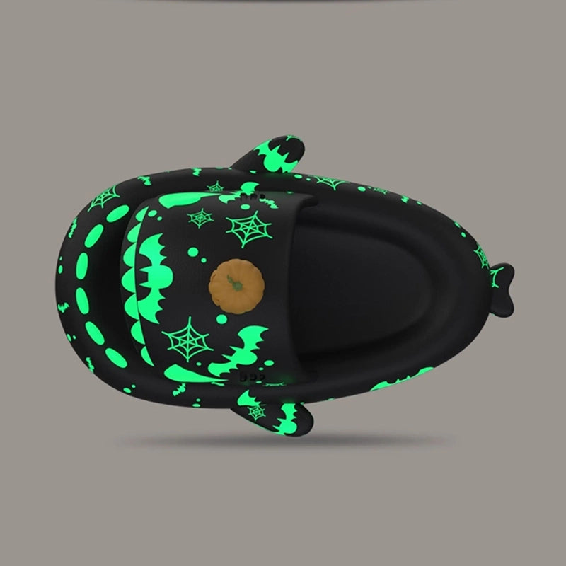 Top-down aerial view of black Halloween shark slides displaying the upper strap layout with glowing green spiderwebs, bats, open-toe shark teeth, side fins, and a 3D pumpkin charm. Top down view of black Cloudsharks Halloween shark slippers with glowing green bat graphics, spiderweb prints, and a 3D pumpkin accent.
